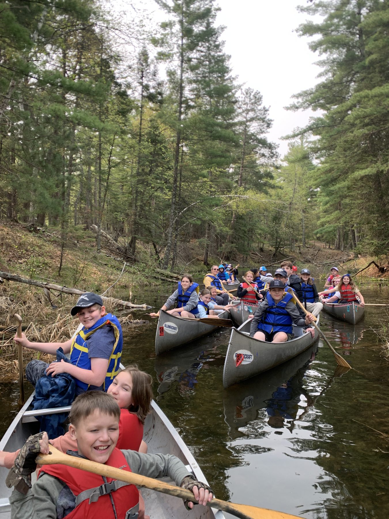 Campers are smiling from several canoes floating in the water at Camp Foley