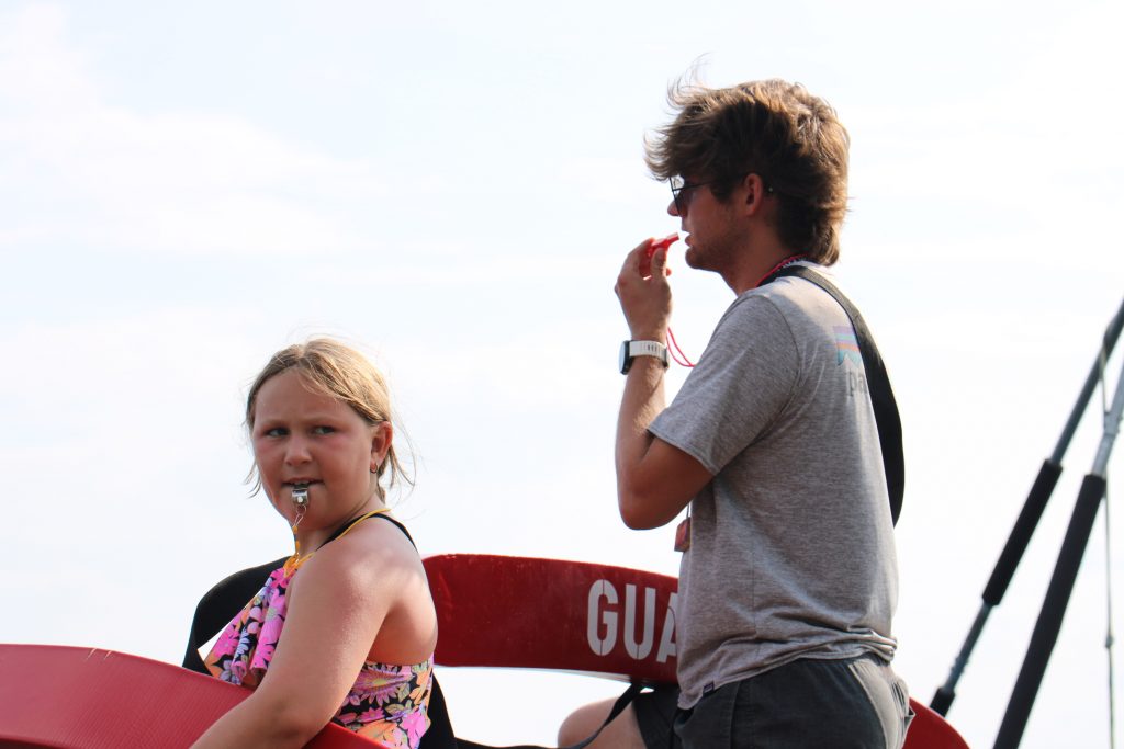 A camper and counselor stand with whistles and life guard tubes 