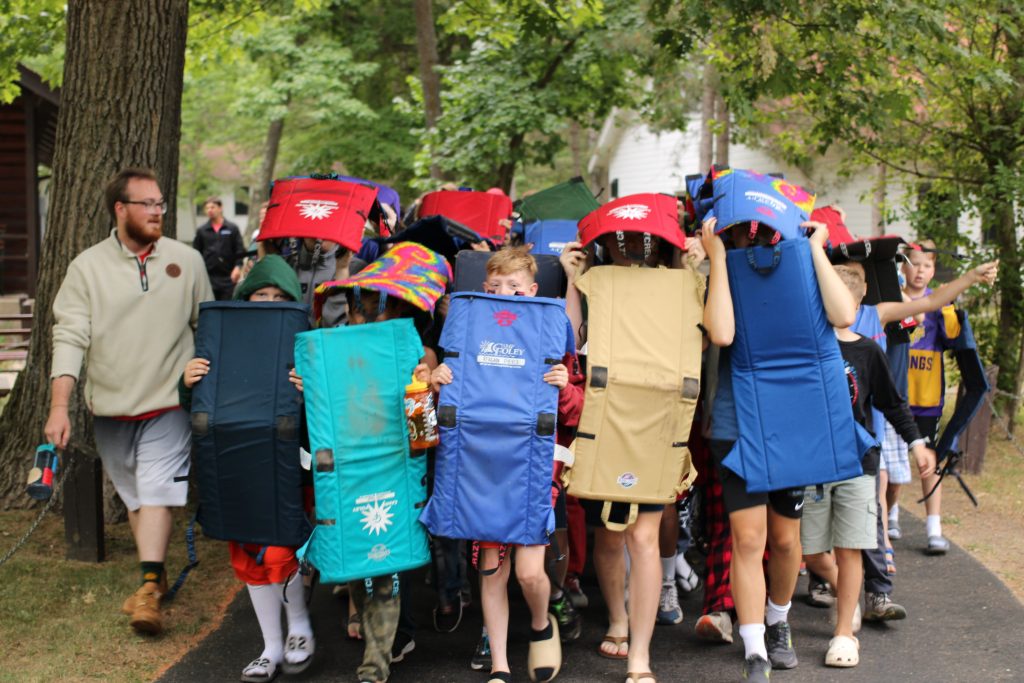 boys walking in a line holding chairs like shields 