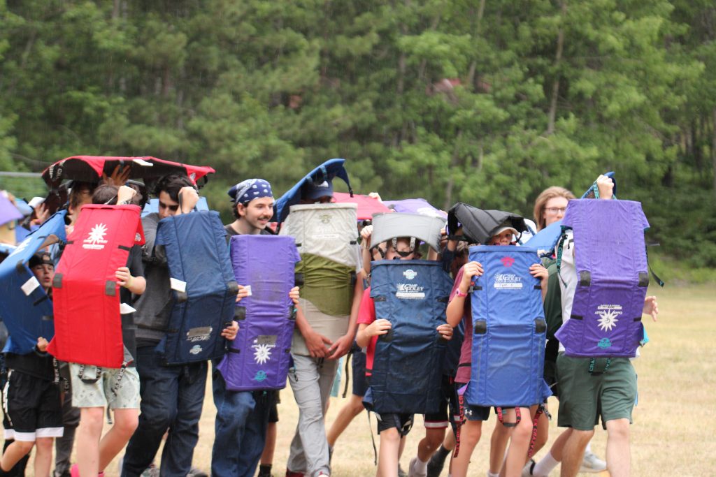 Boys walking in a line holding camp chairs as shields 