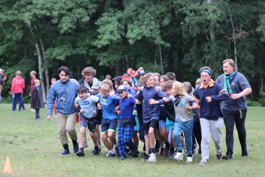 Boys in blue with linked arms running in a straight line at Camp Foley