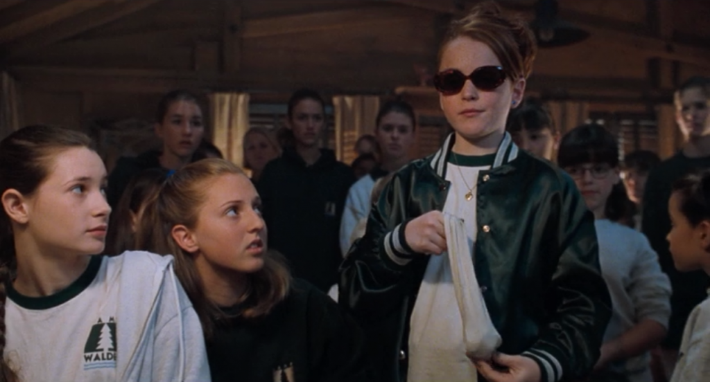 Girl campers look on as a girl wearing sunglasses holds a sock full of coins 