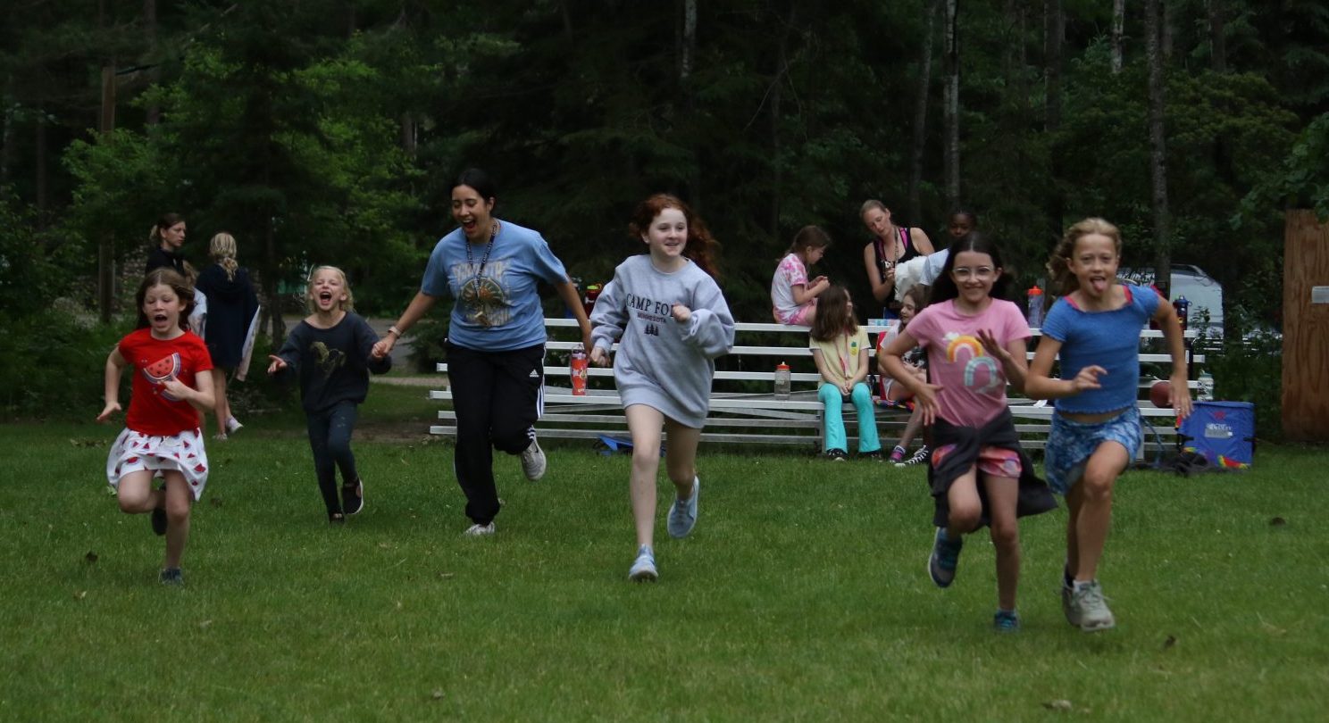 A group of young girls and one adult run towards the camera smiling 