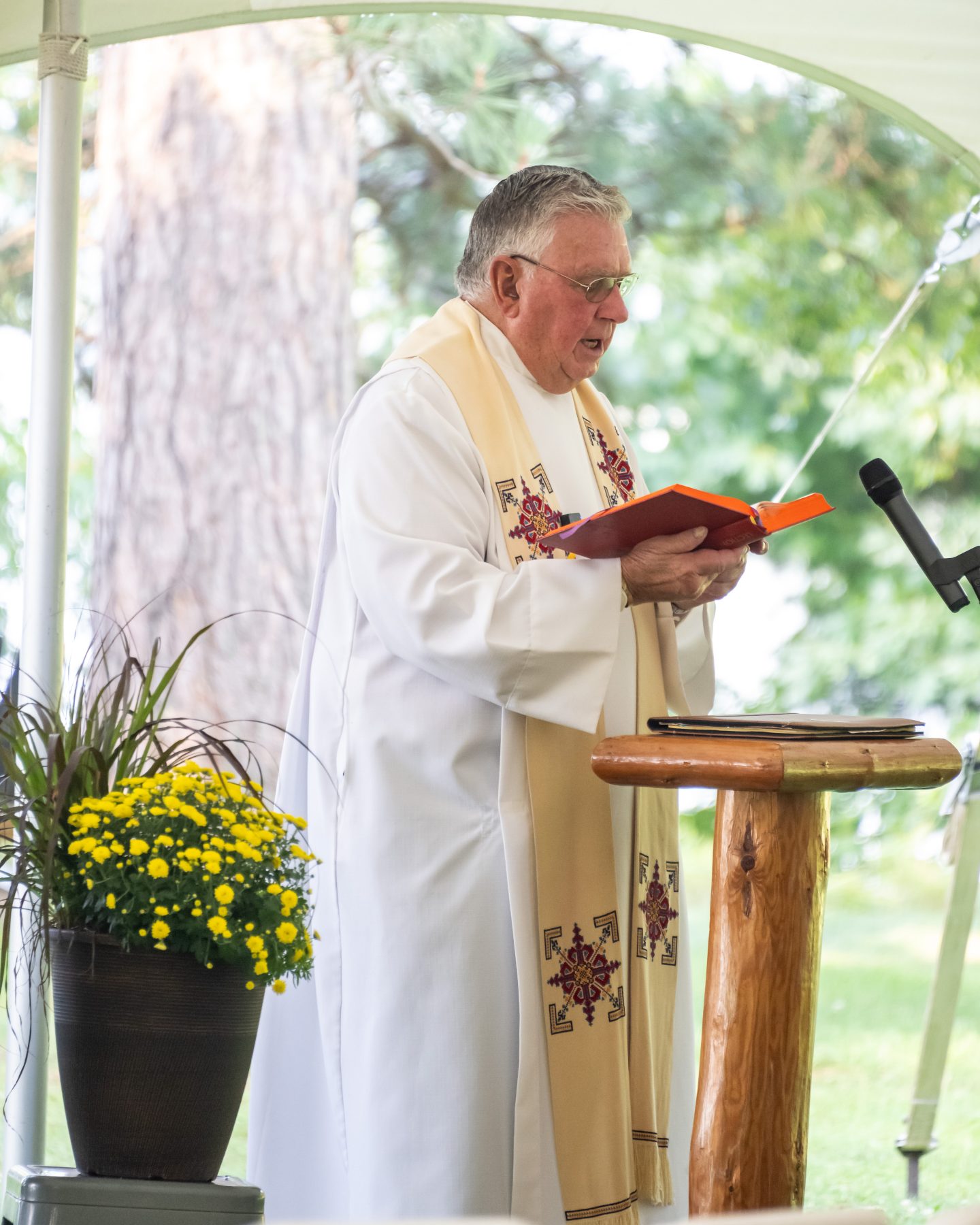 A man in priest robes stands at a podium holding a book 