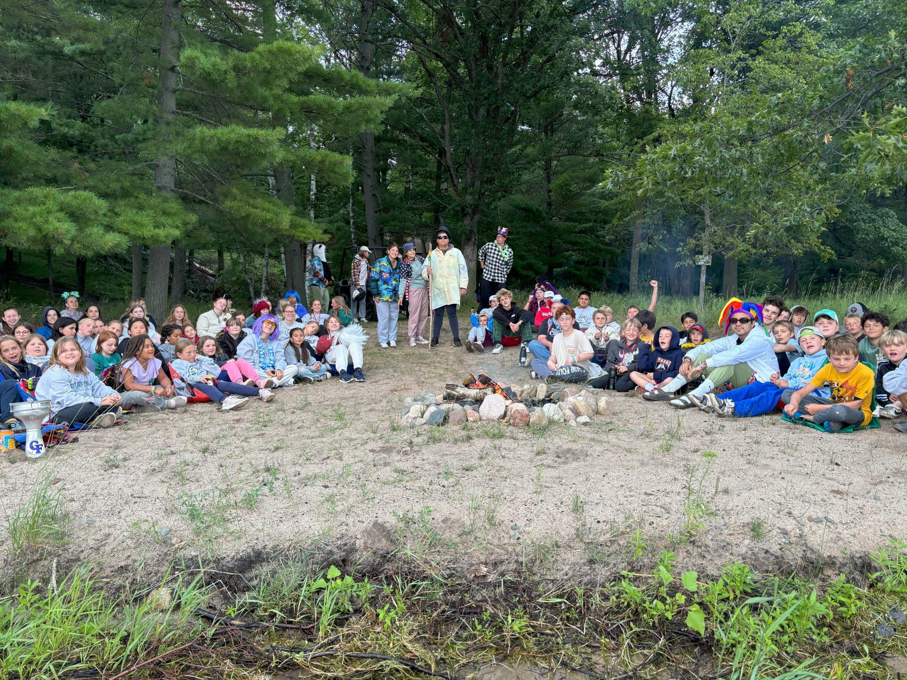 A group of campers and staff sit on a beach attending a campfire 