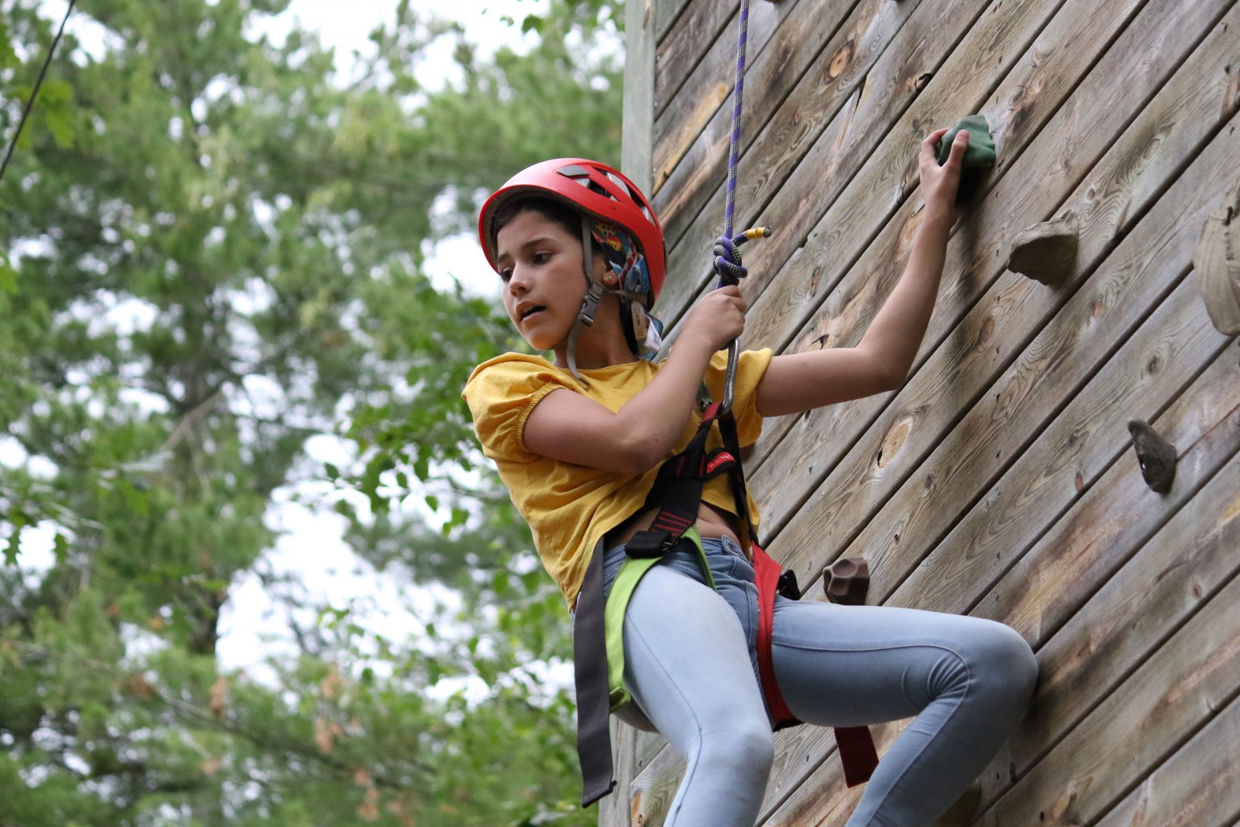 A girl climbs the Camp Foley climbing wall with a red helmet on 