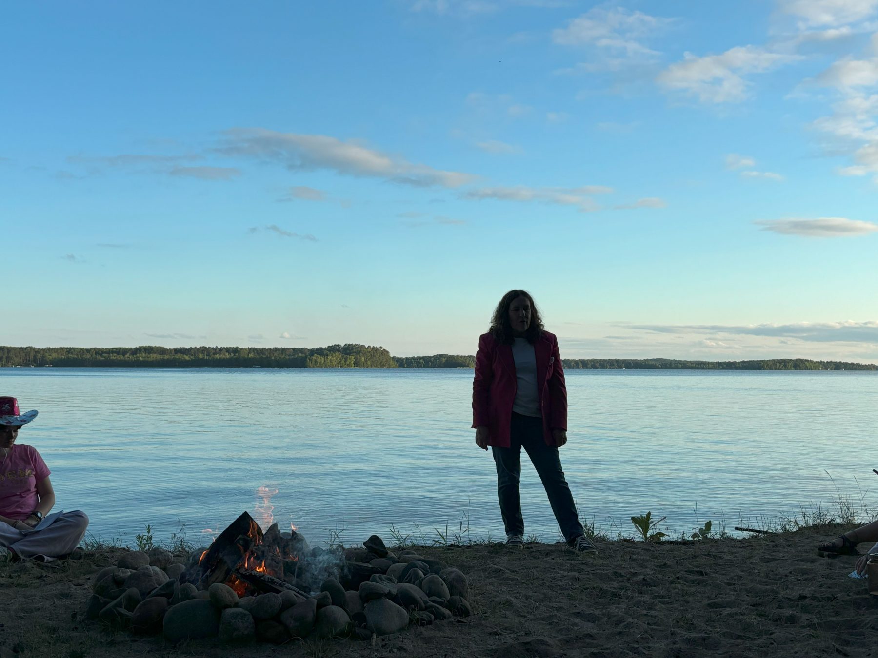 A woman in a pink blazer stands in front of a lake 