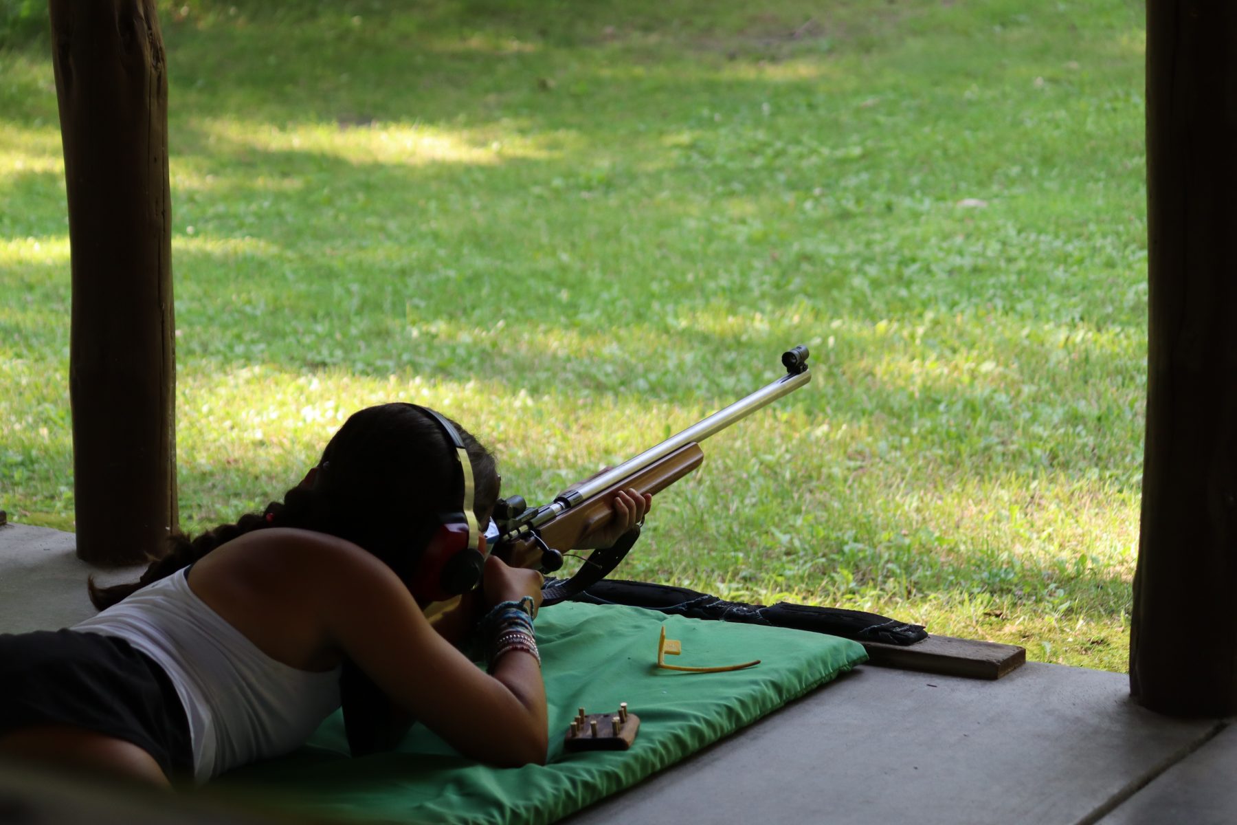 A girl camper aims a rifle down range in the prone position 