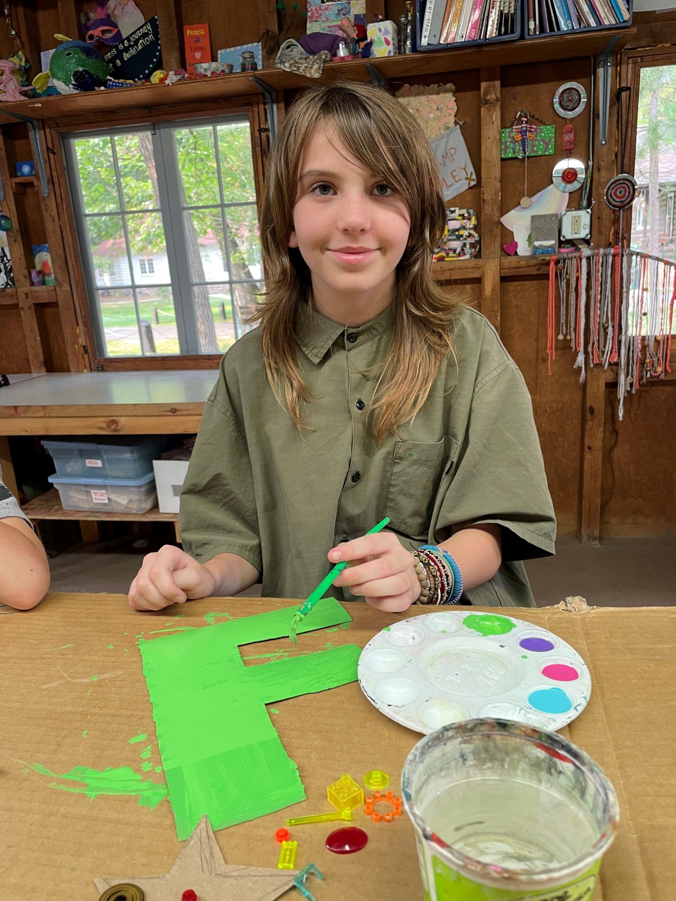 A girl sits in the Camp Foley crafts building painting an F