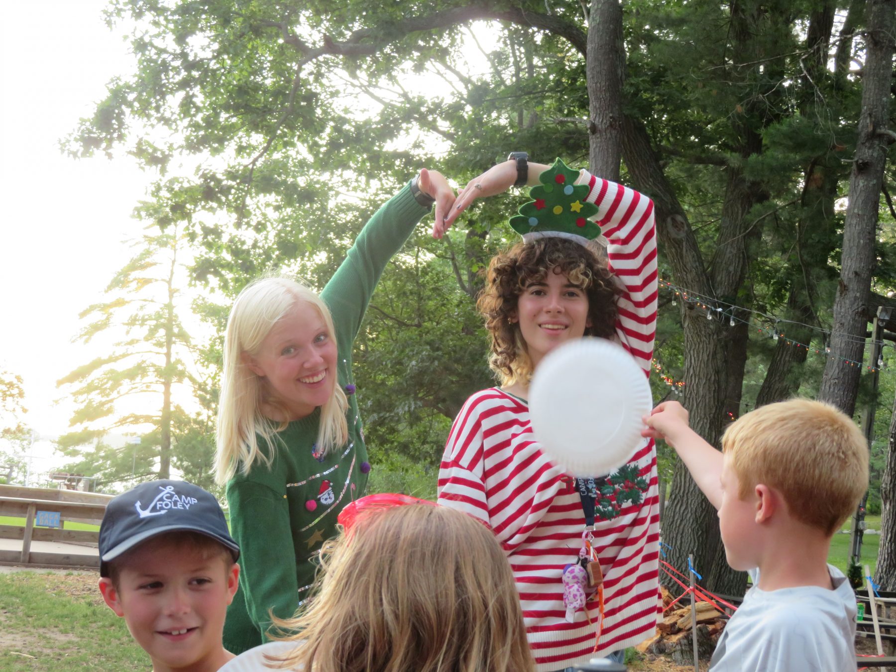 2 girls pose in Christmas sweaters at Camp Foley, making a heart with their arms 