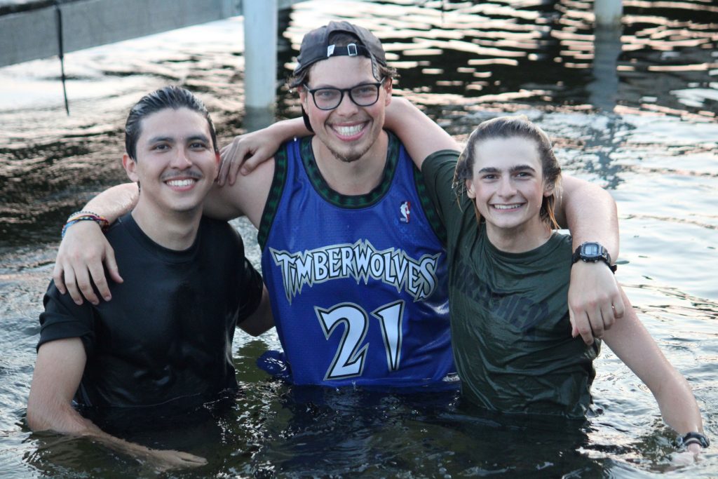 3 male Camp Foley staff smile at the camera in the lake 