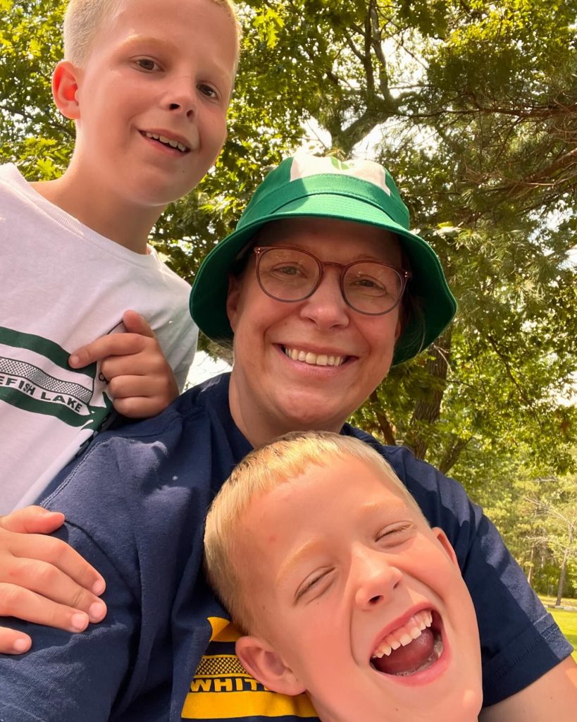 A mother wears a green Foley bucket hat and smiles with her two sons 